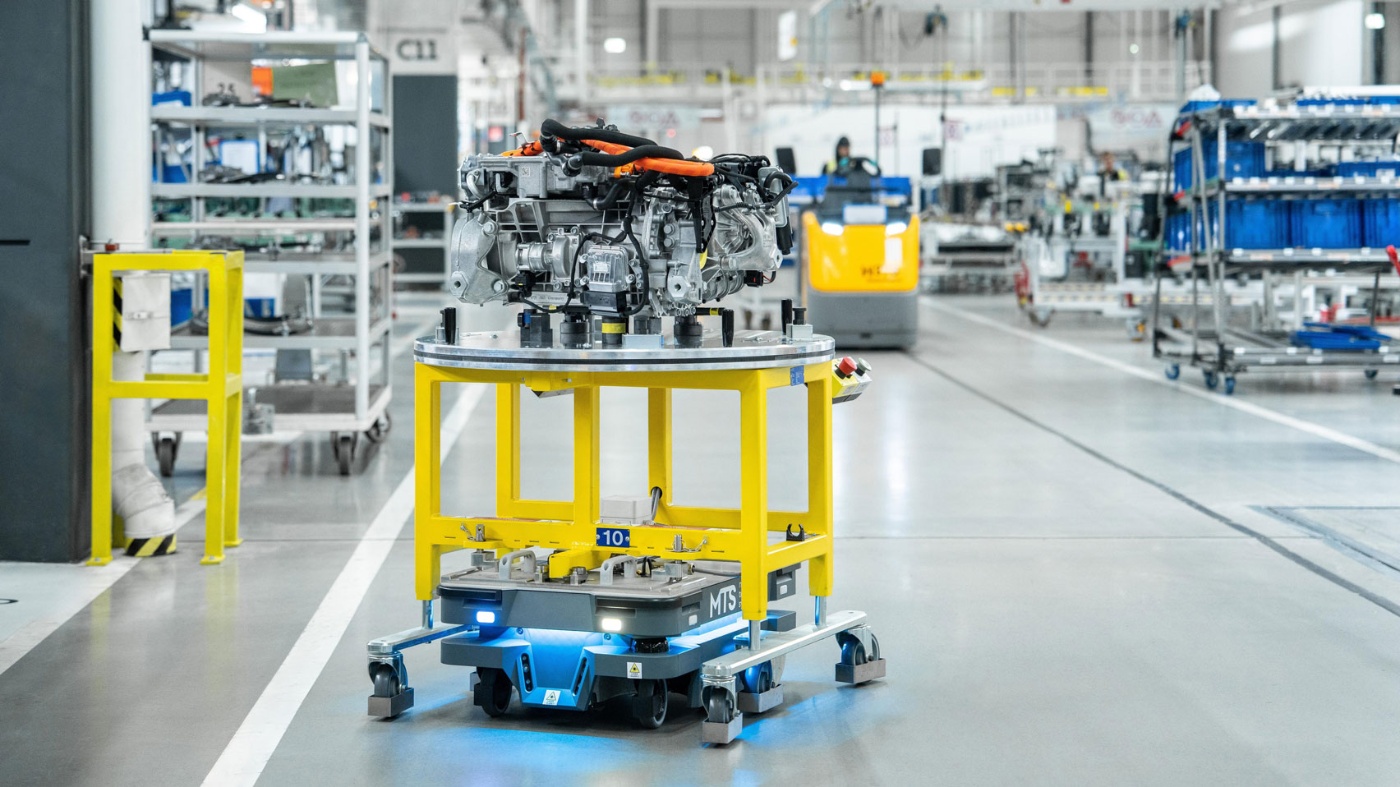 Autonomer Roboter transportiert ein Motormodul durch eine moderne Fabrikhalle.