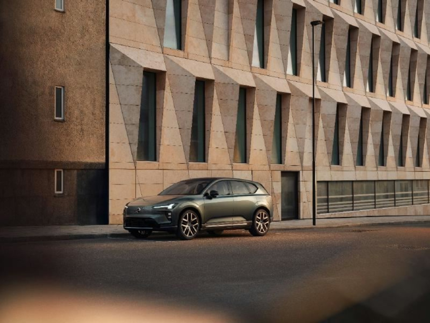 Elektrischer SUV steht auf leerer Straße vor modernem Gebäude mit geometrischen Fenstern.
