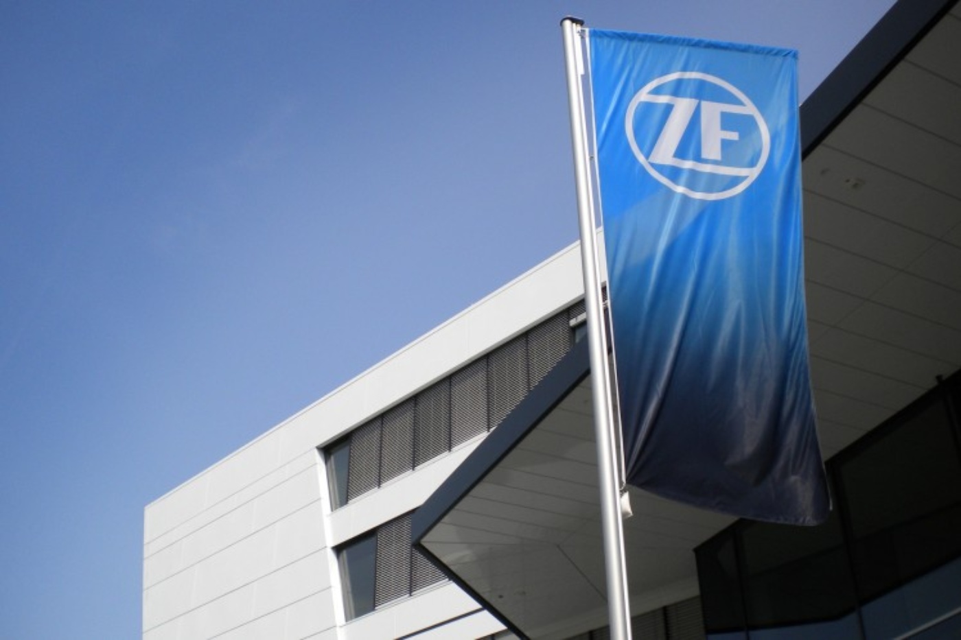 Blaue ZF-Flagge vor einem modernen Bürogebäude mit weißer Fassade.