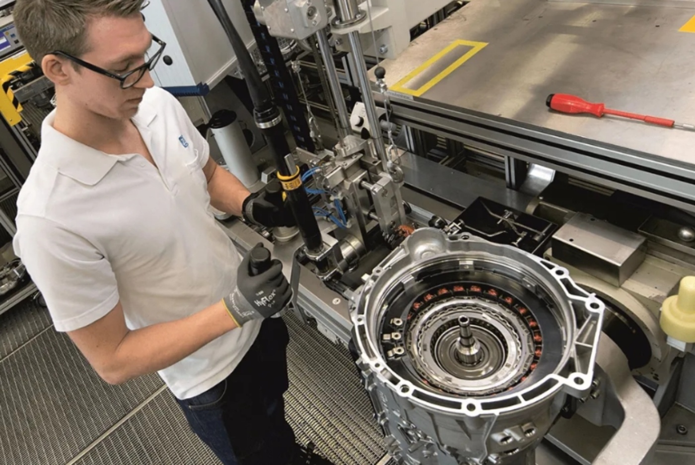 Techniker montiert ein Getriebeteil an einer Werkbank in industrieller Umgebung.