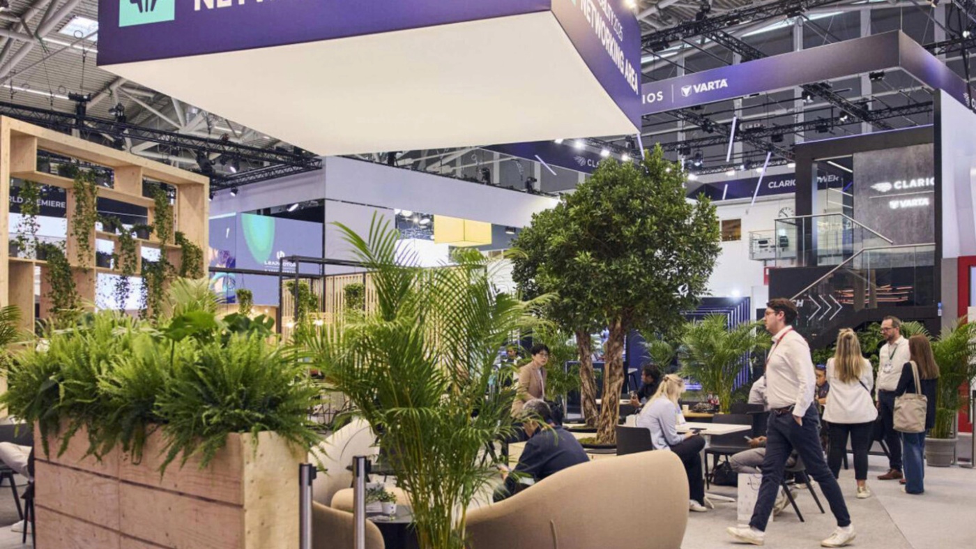 Visitors meet in a networking area with seating and plants at a trade show.