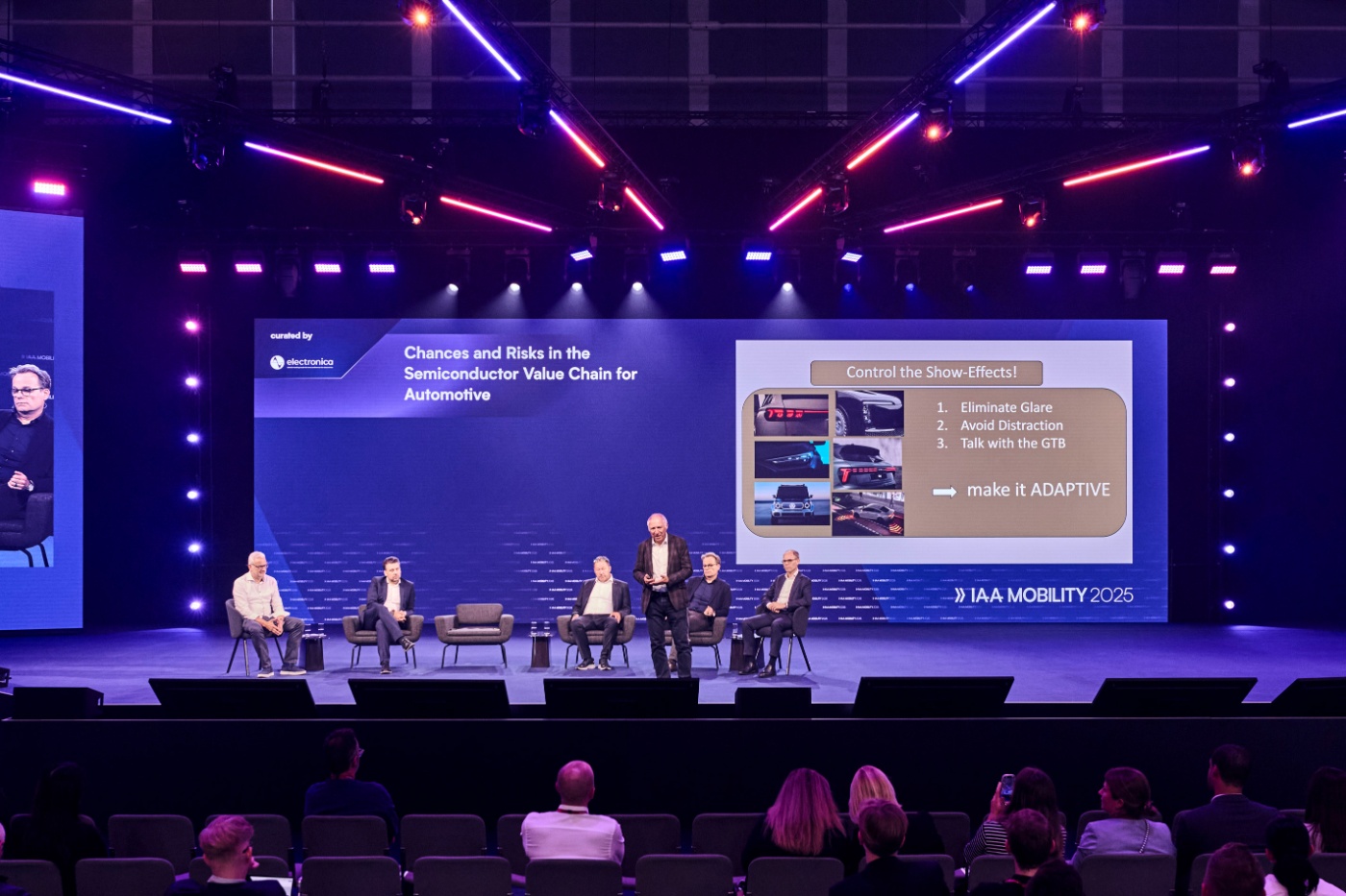 Podiumsdiskussion auf einer Konferenzbühne mit großer Präsentationsleinwand.
