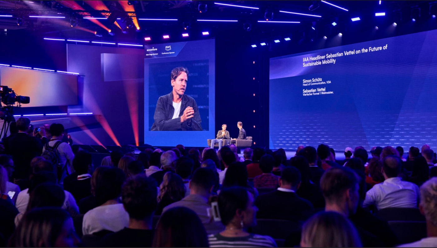 Publikum verfolgt Redner auf der Bühne während einer Konferenz.