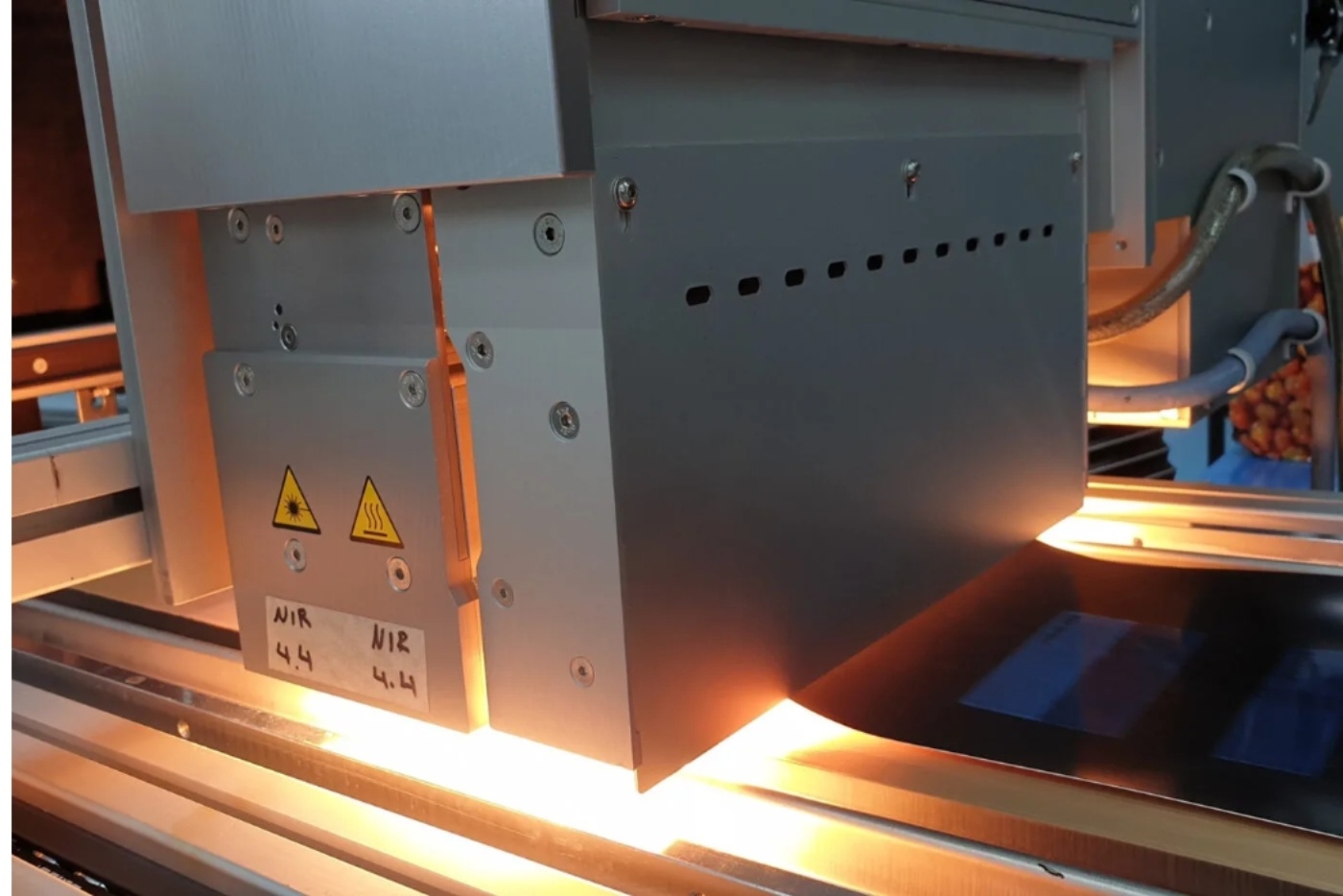Close-up of an industrial near-infrared (NIR) inspection or heating unit in operation, illuminating a conveyor belt with strong light.