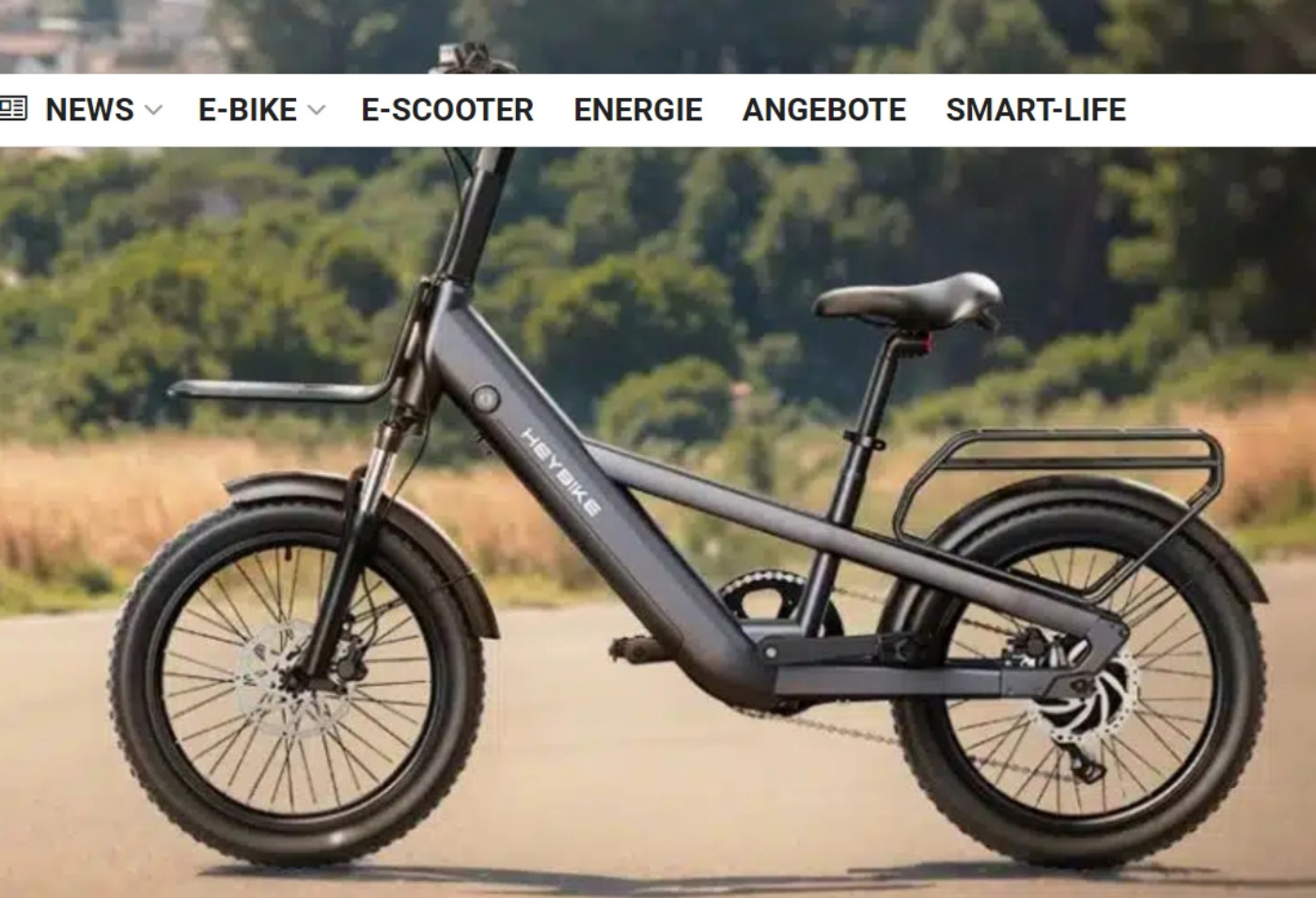 Side view of a modern electric bicycle with thick tires, labeled "Heybike", parked on a road with trees and fields in the background.
