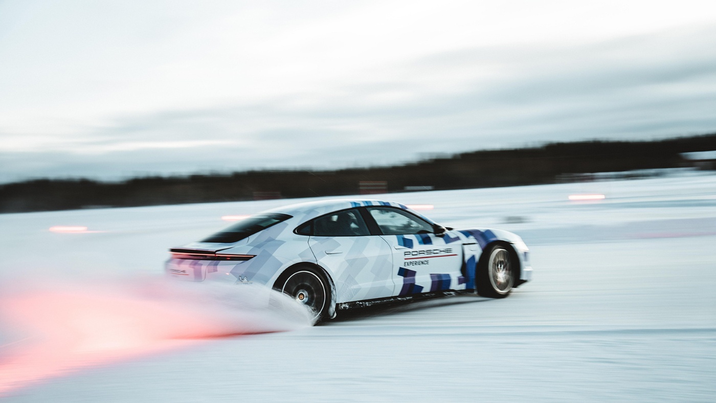 A sports car with dynamic markings drifts at high speed across a snowy track, kicking up snow with glowing red tail lights.