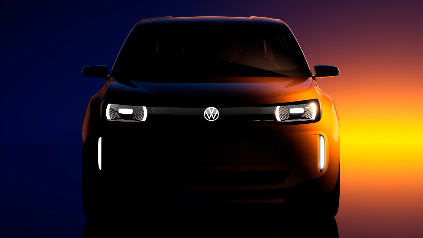 Frontansicht eines Volkswagen-Konzeptfahrzeugs mit beleuchteten Scheinwerfern und Logo vor einem Sonnenuntergang im dramatischen Licht.