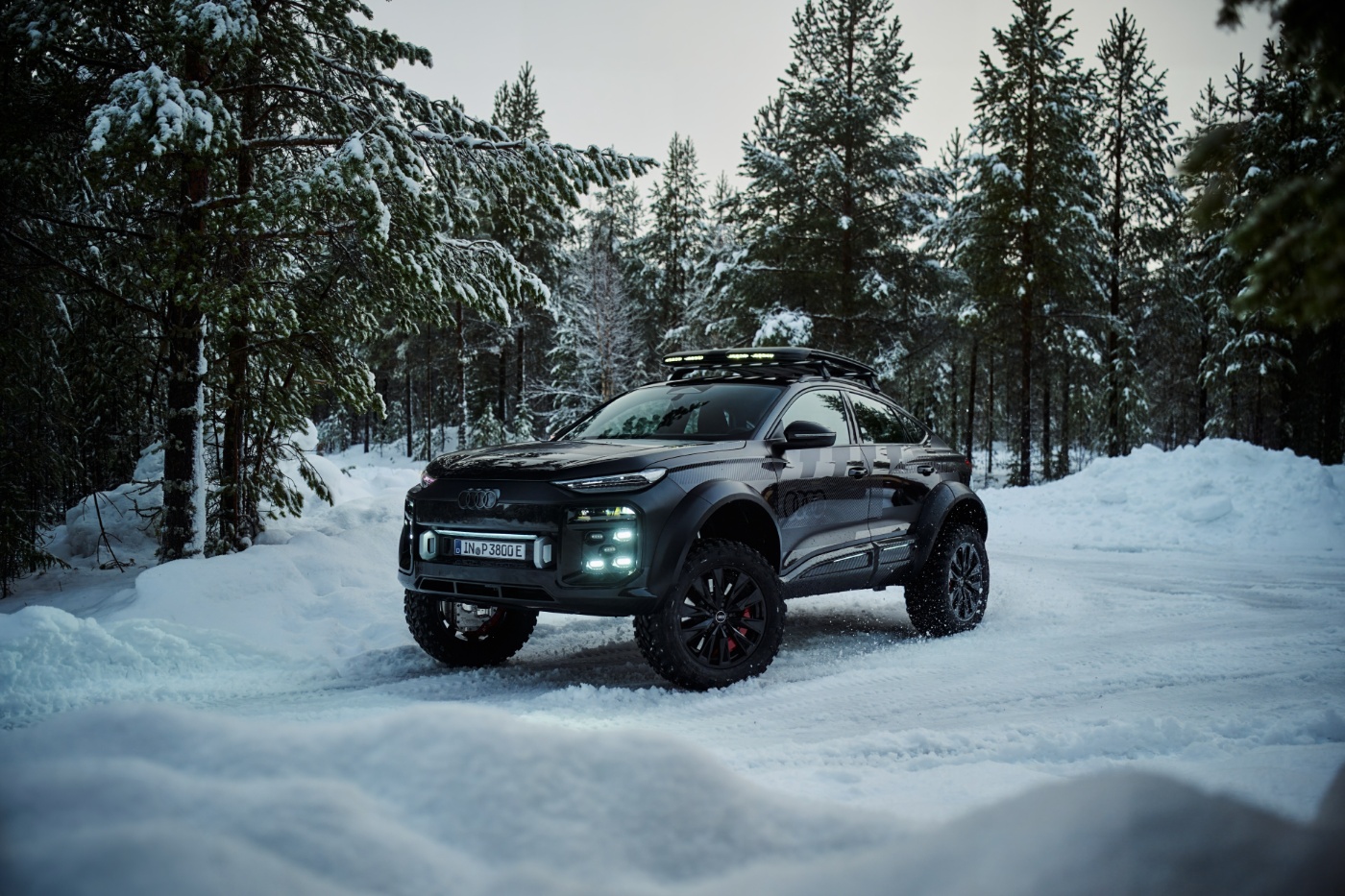 Schwarzer, modifizierter Audi-SUV mit Offroad-Reifen und Dachbeleuchtung auf einer verschneiten Waldstraße.