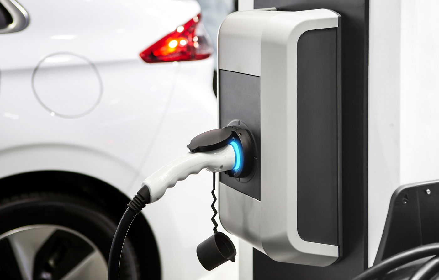 Close-up of an electric car charging at a station, with the plug connected and a glowing blue light indicating charging status.