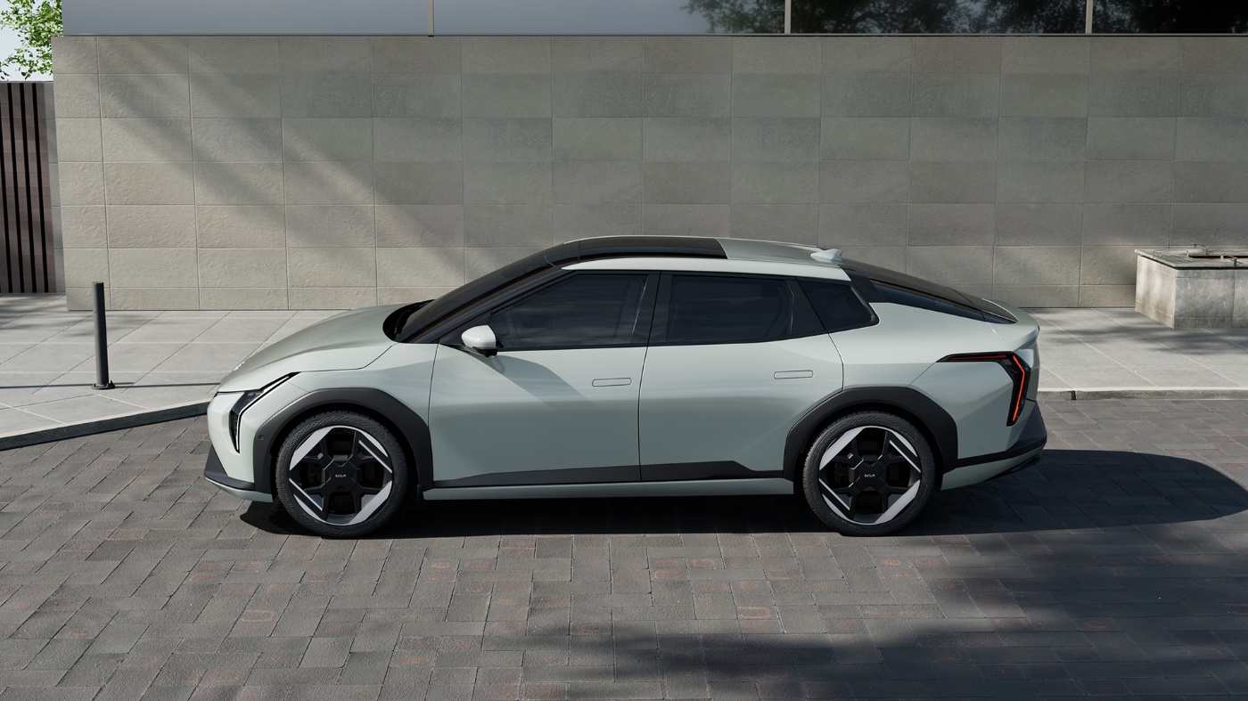 Side view of a modern electric crossover vehicle parked on a paved urban street in front of a plain stone wall.