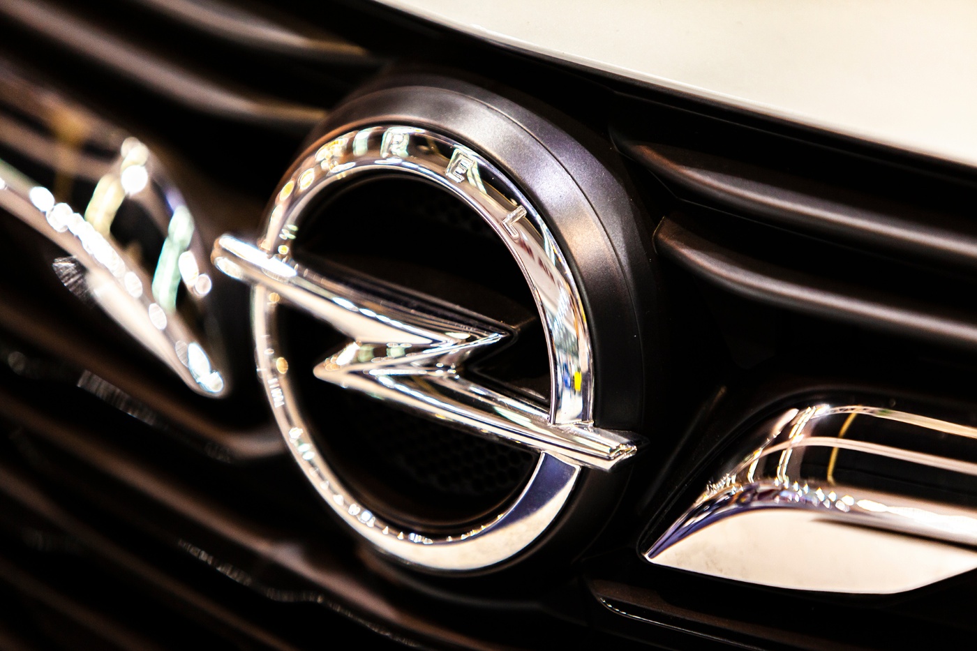 Close-up of the shiny Opel logo on the front grille of a vehicle, showing chrome details and reflections.
