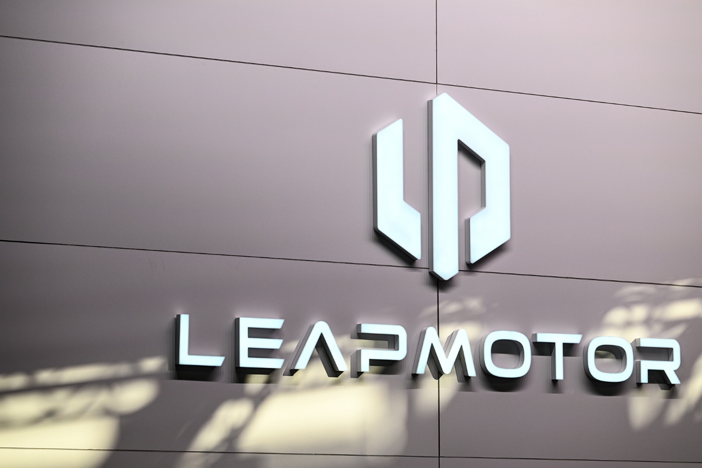 Illuminated Leapmotor logo on a light gray wall, with soft shadows from overhead lighting.