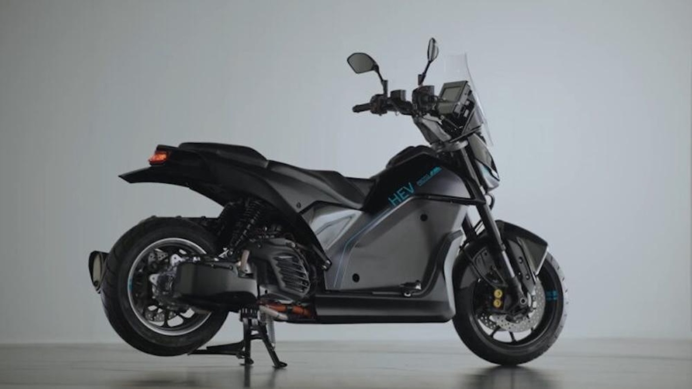 Side view of a black and grey Yamaha hybrid electric scooter standing on a kickstand in a studio setting.