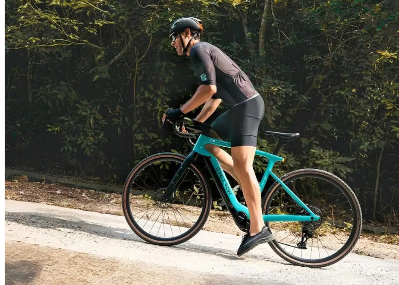 A cyclist in sportswear rides a turquoise Cyctron electric bike uphill on a forest road.