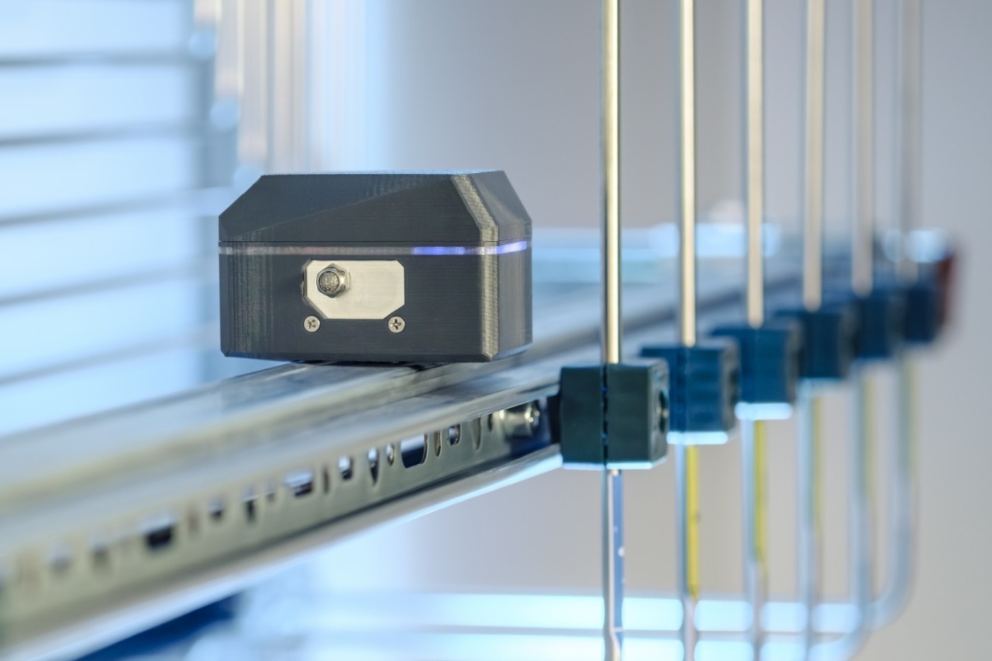 Close-up of a sensor or measurement device mounted on a metal rail system in a lab environment.