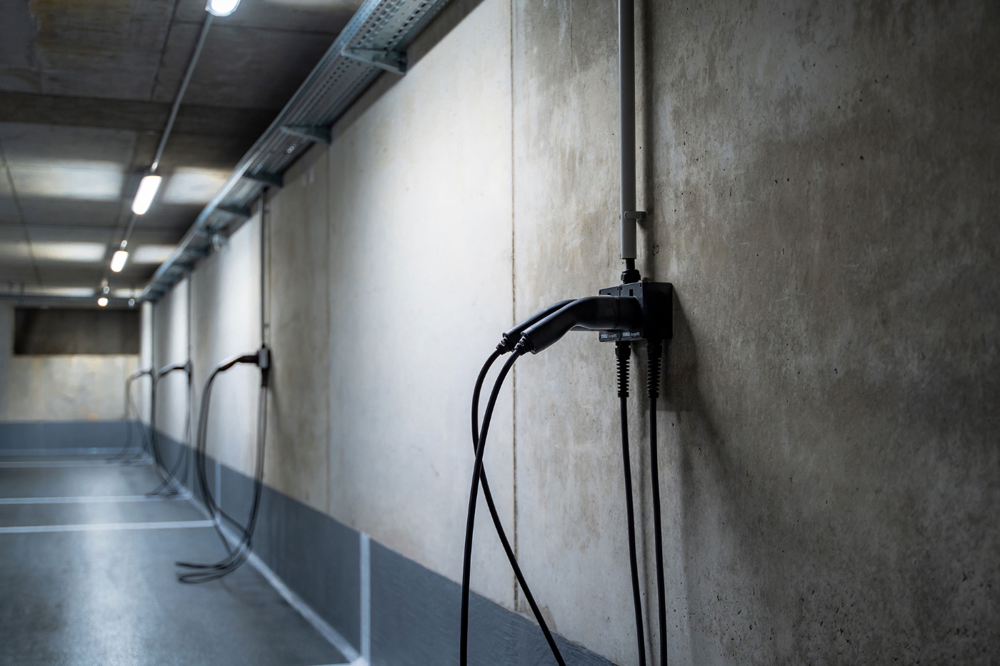 Wall-mounted EV charging cables in an empty parking garage, viewed from the side.