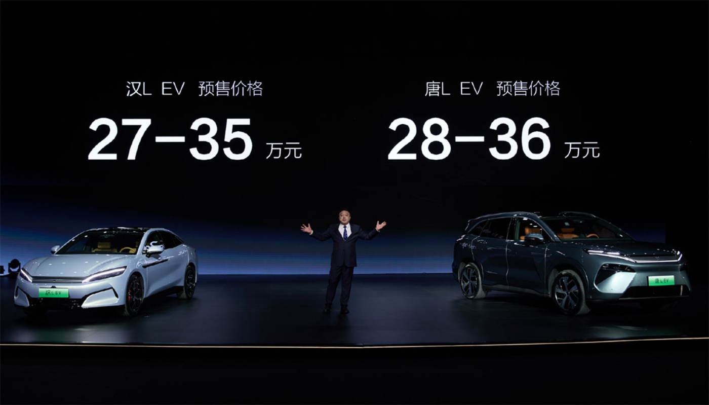 Präsentation von zwei elektrischen BYD-Fahrzeugen auf einer Bühne, mit einem Sprecher in der Mitte und chinesischen Preisangaben über den Autos.