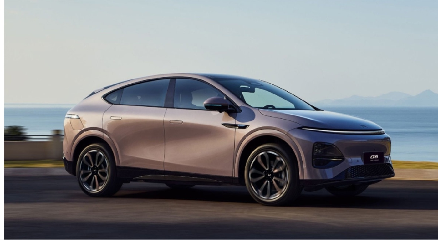 Seitenansicht eines eleganten XPeng G6 Elektro-SUVs auf einer Küstenstraße mit Meer und Bergen im Hintergrund.