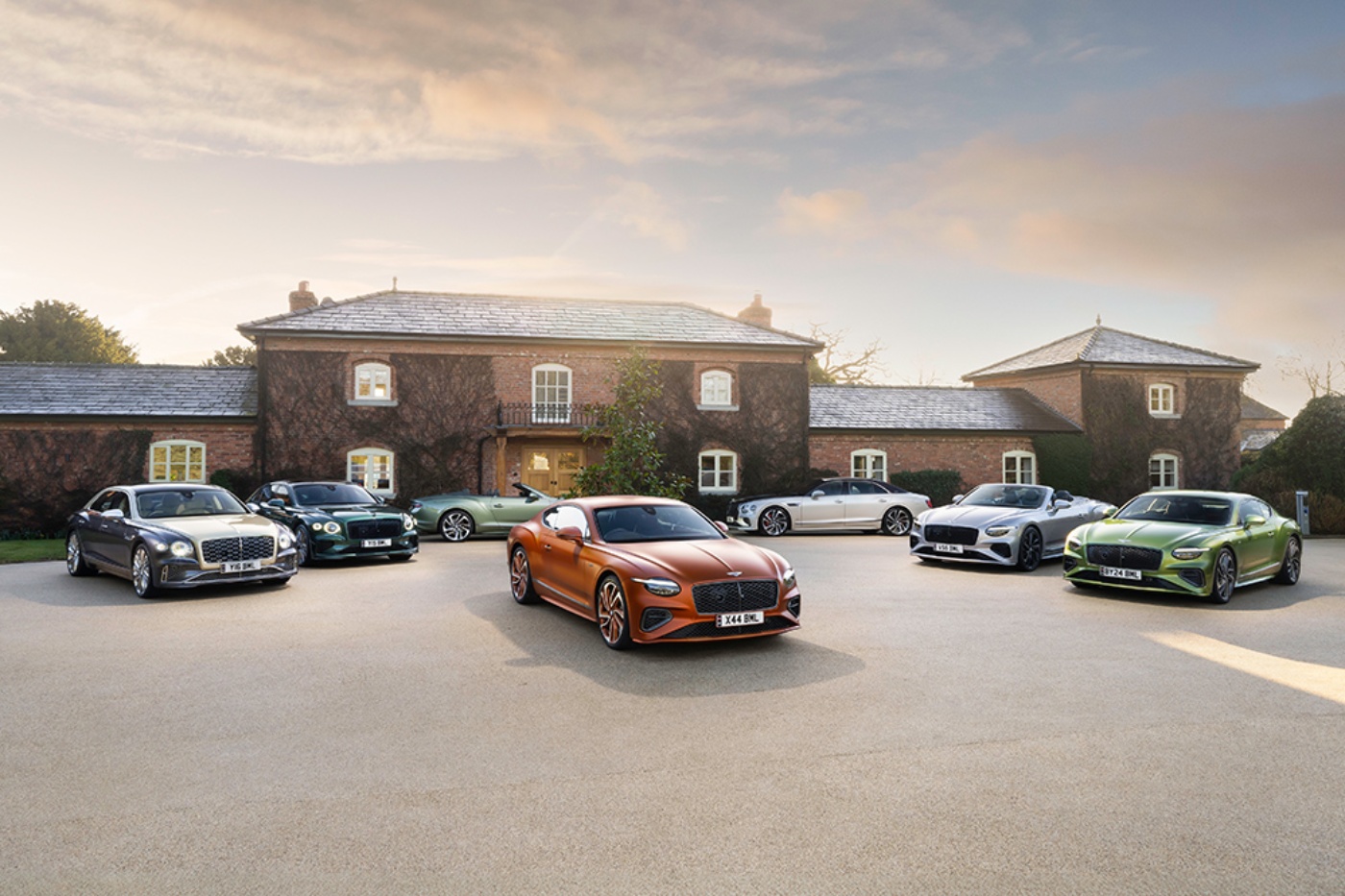 Mehrere Luxusautos stehen auf einer runden Auffahrt vor einer großen Villa aus Backstein.