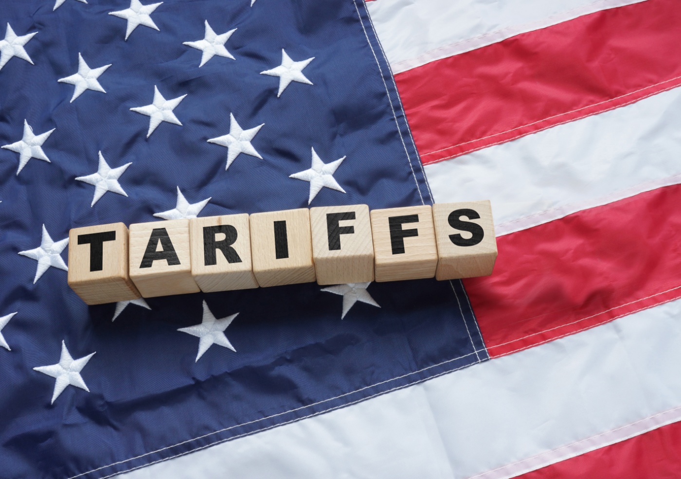 Holzbuchstaben mit dem Wort „TARIFFS“ liegen auf einer US-Flagge und symbolisieren amerikanische Handelspolitik oder Einfuhrzölle.