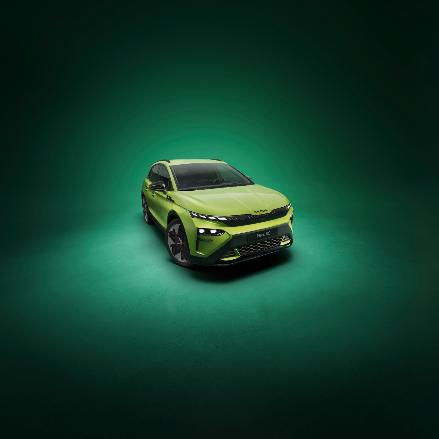 Frontansicht eines grünen Škoda-Elektroautos vor dunkelgrünem Hintergrund, im Studio beleuchtet zur Betonung des Fahrzeugdesigns.