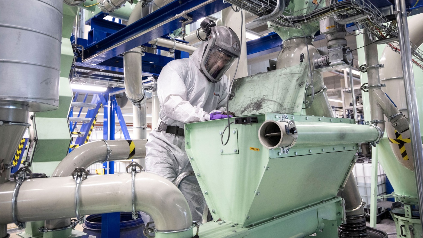 Arbeiter in Schutzanzug und Helm bedient eine Maschine in einer industriellen Recyclinganlage.