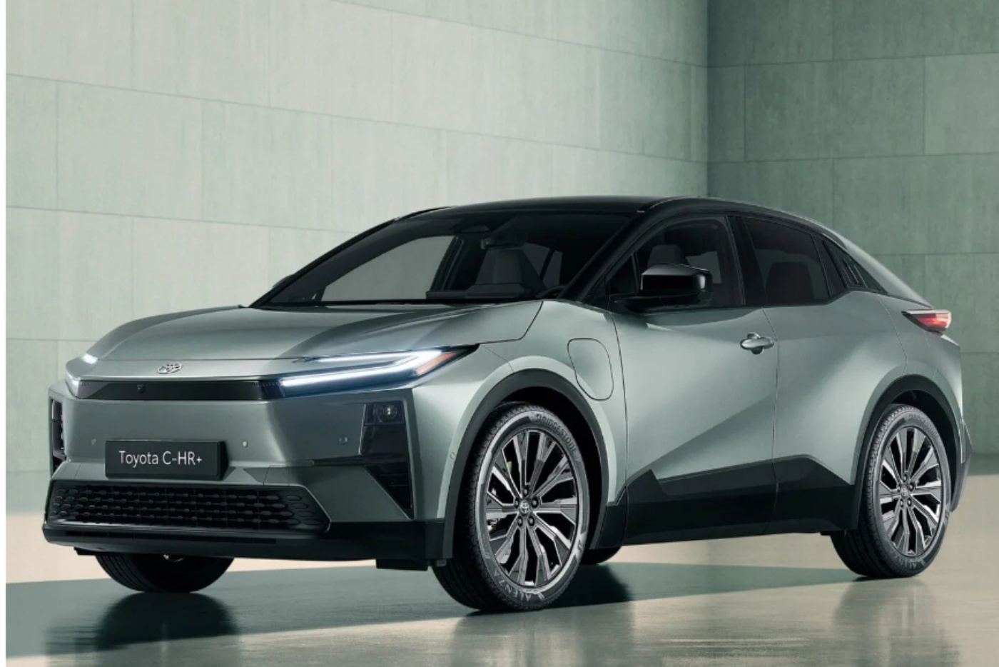 Front- und Seitenansicht eines silbernen Toyota C-HR Plug-in-Hybrids in einer schlichten Innenraumumgebung.