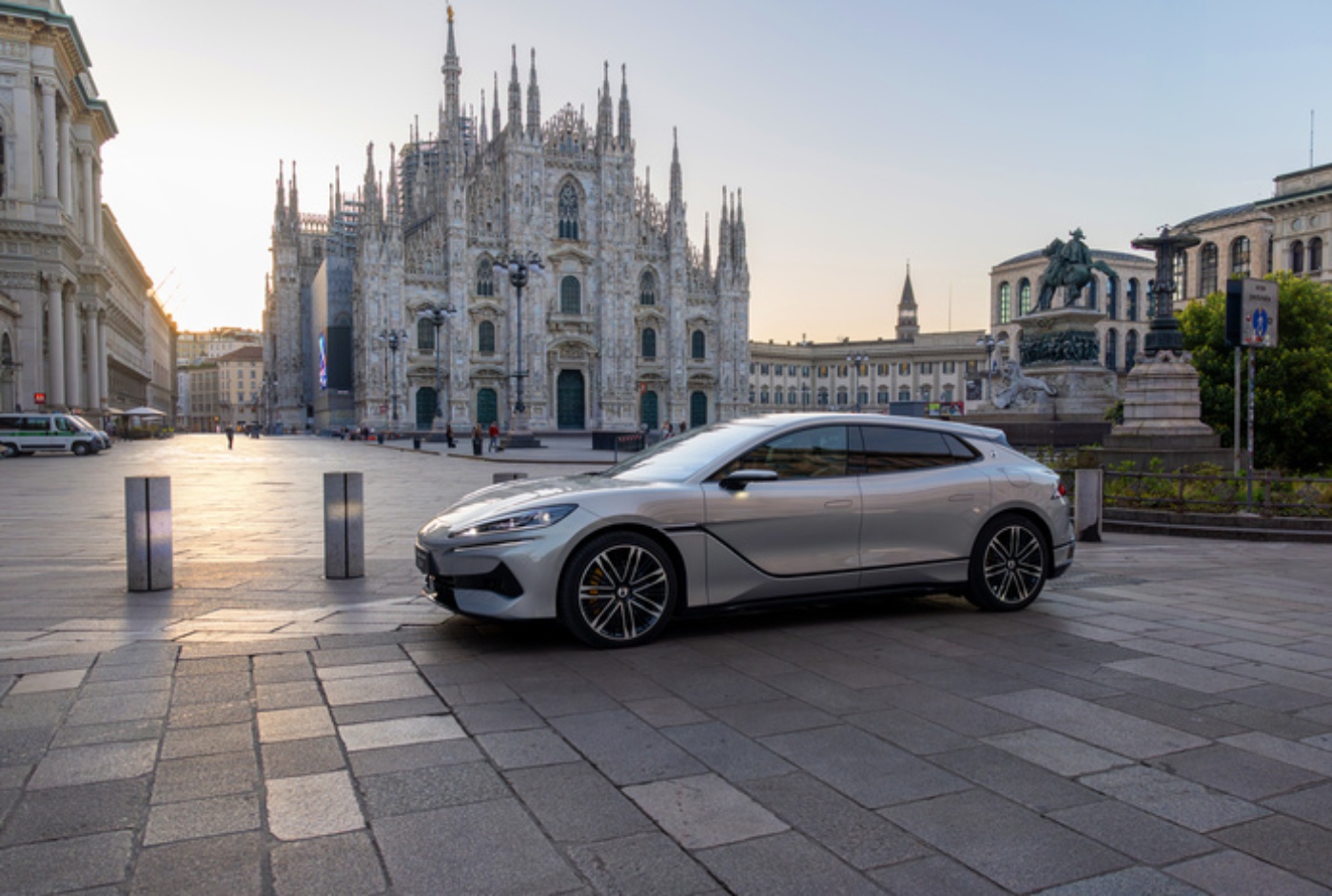 Silbernes Elektroauto steht bei Sonnenaufgang auf einem historischen Platz vor dem Mailänder Dom.