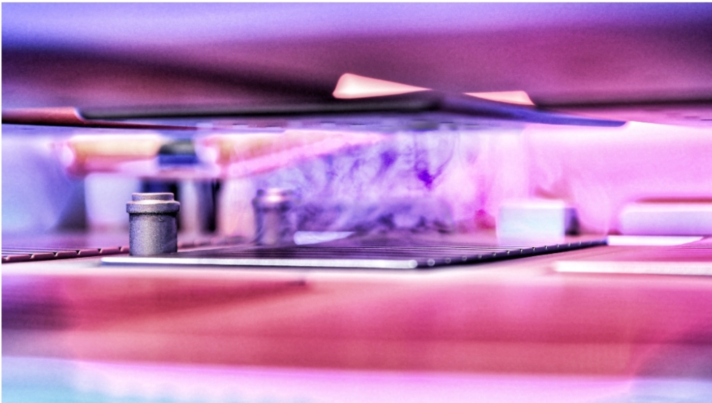 Close-up view of a manufacturing process with components under a heated press, shown in pink and purple lighting.