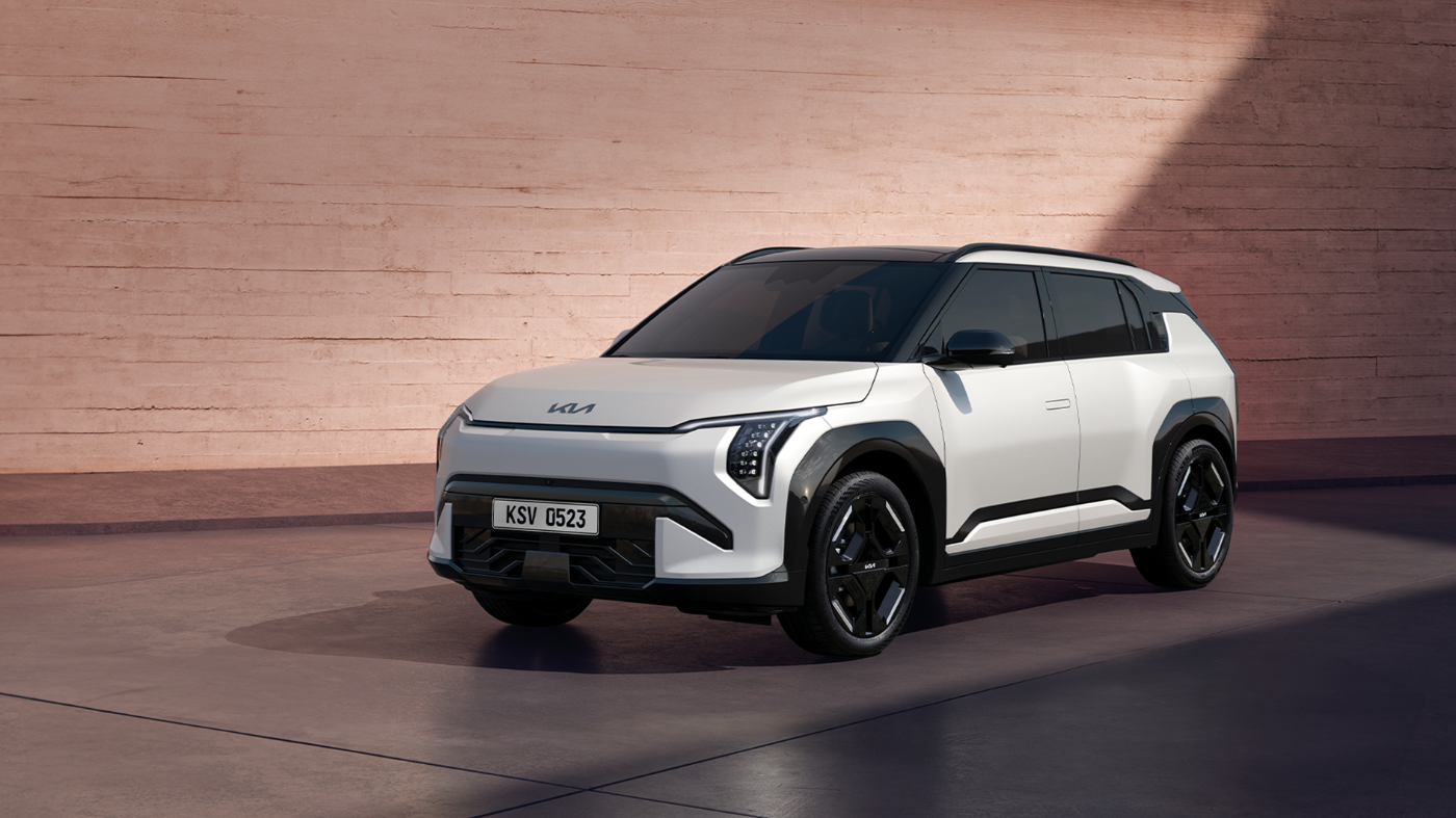 Electric SUV from Kia parked in front of a modern concrete wall, shown in a well-lit outdoor setting.