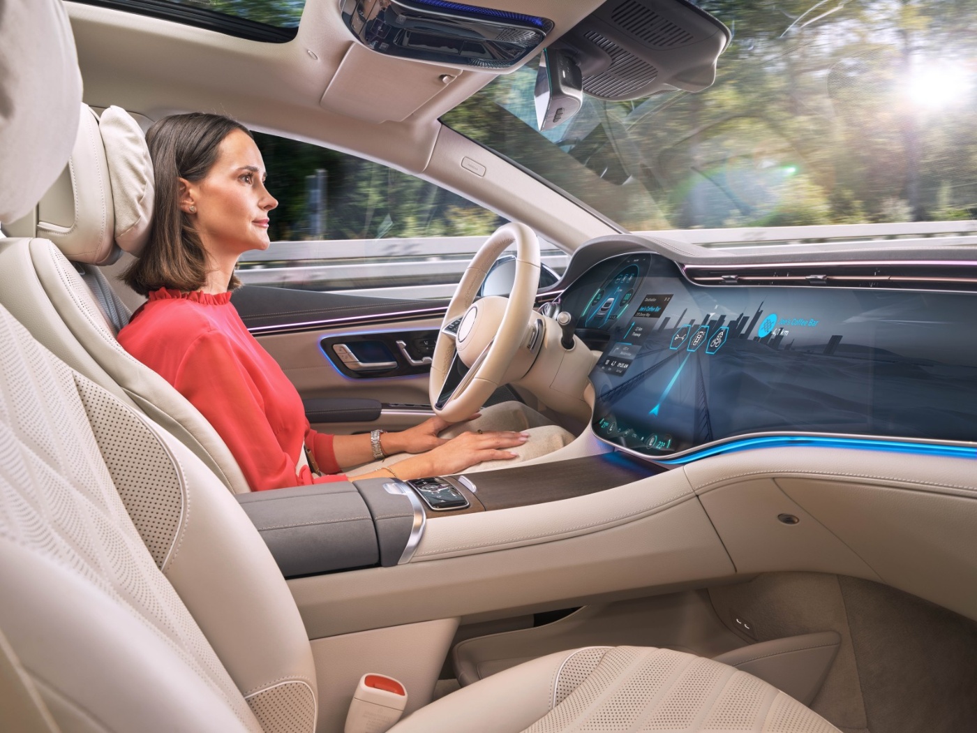 Eine Frau sitzt entspannt auf dem Fahrersitz eines modernen Autos mit großem digitalen Display, das Navigation und Fahrzeugdaten anzeigt.