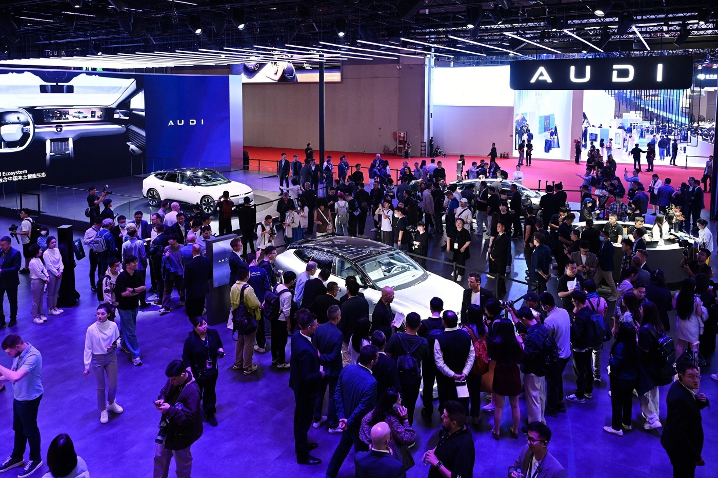 Eine große Menschenmenge versammelt sich am Audi-Messestand, wo mehrere Elektrofahrzeuge unter heller Beleuchtung und großen Bildschirmen ausgestellt sind.