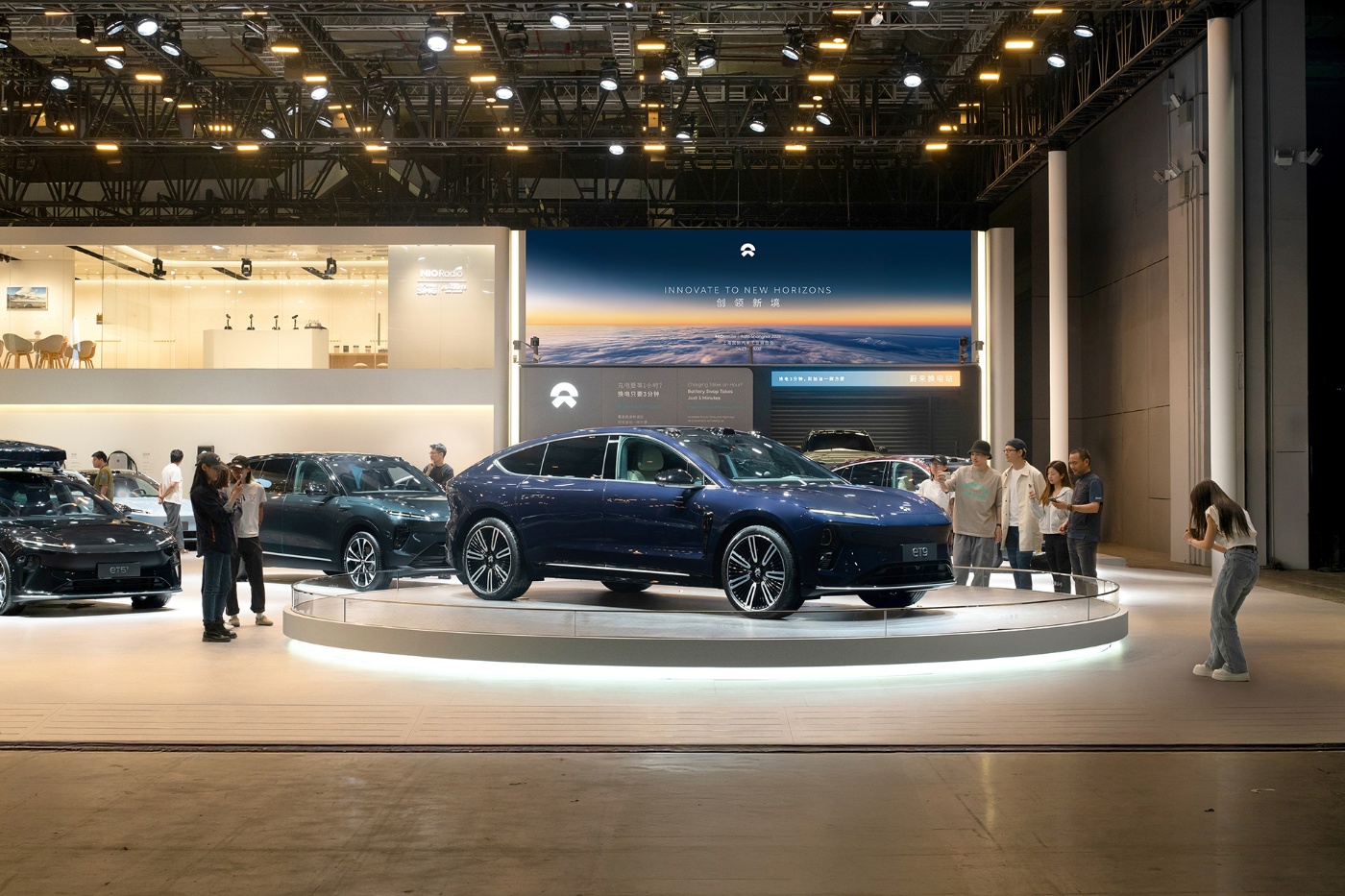 Ein dunkelblauer elektrischer SUV von NIO steht auf einer runden Plattform bei einer Automobilausstellung, umgeben von Besucher