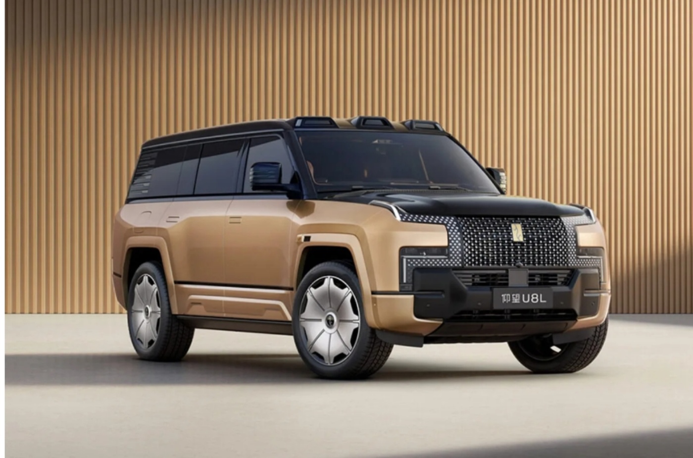 Ein großer, gold-schwarzer Luxus-SUV mit kantigem Design steht vor einer hell gerippten Wand und trägt den Schriftzug U8L auf dem Kennzeichen.