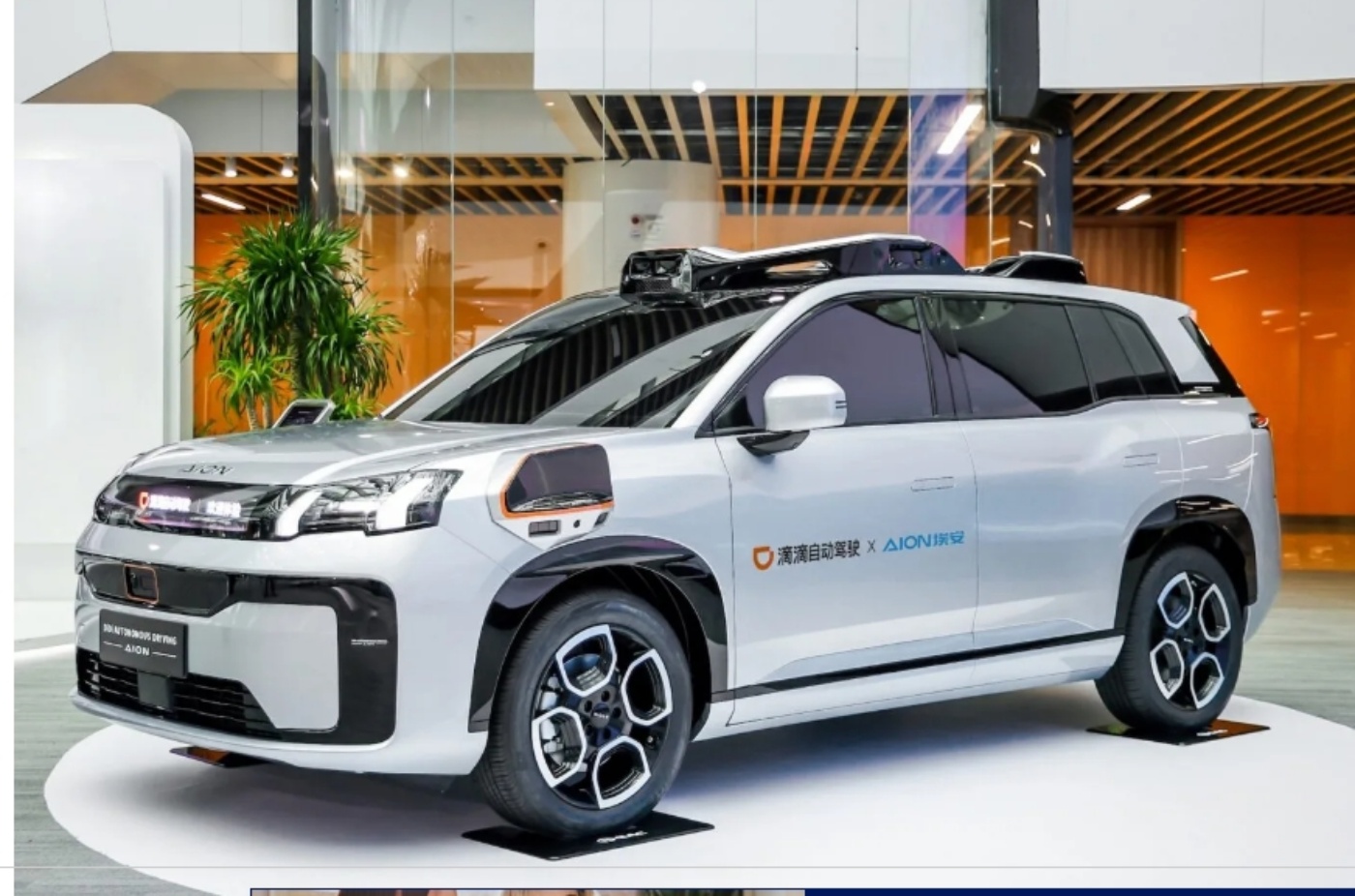 Ein weißes autonomes SUV mit montierten Sensoren und Logos von Didi und Aion steht in einem modernen Ausstellungsraum.