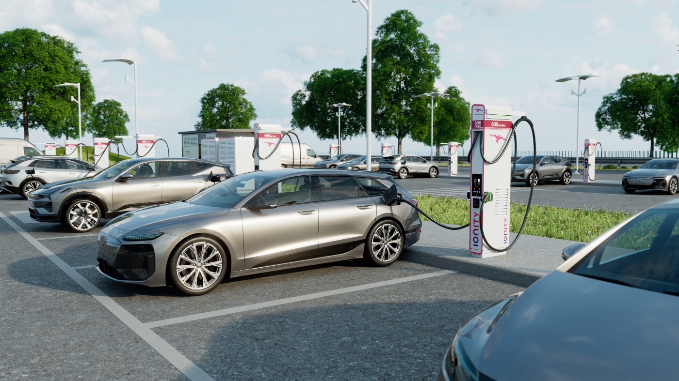 Mehrere Elektroautos stehen an einer Ladestation, wobei ein Auto im Vordergrund an eine Ionity-Schnellladesäule angeschlossen ist, bei sonnigem Wetter.