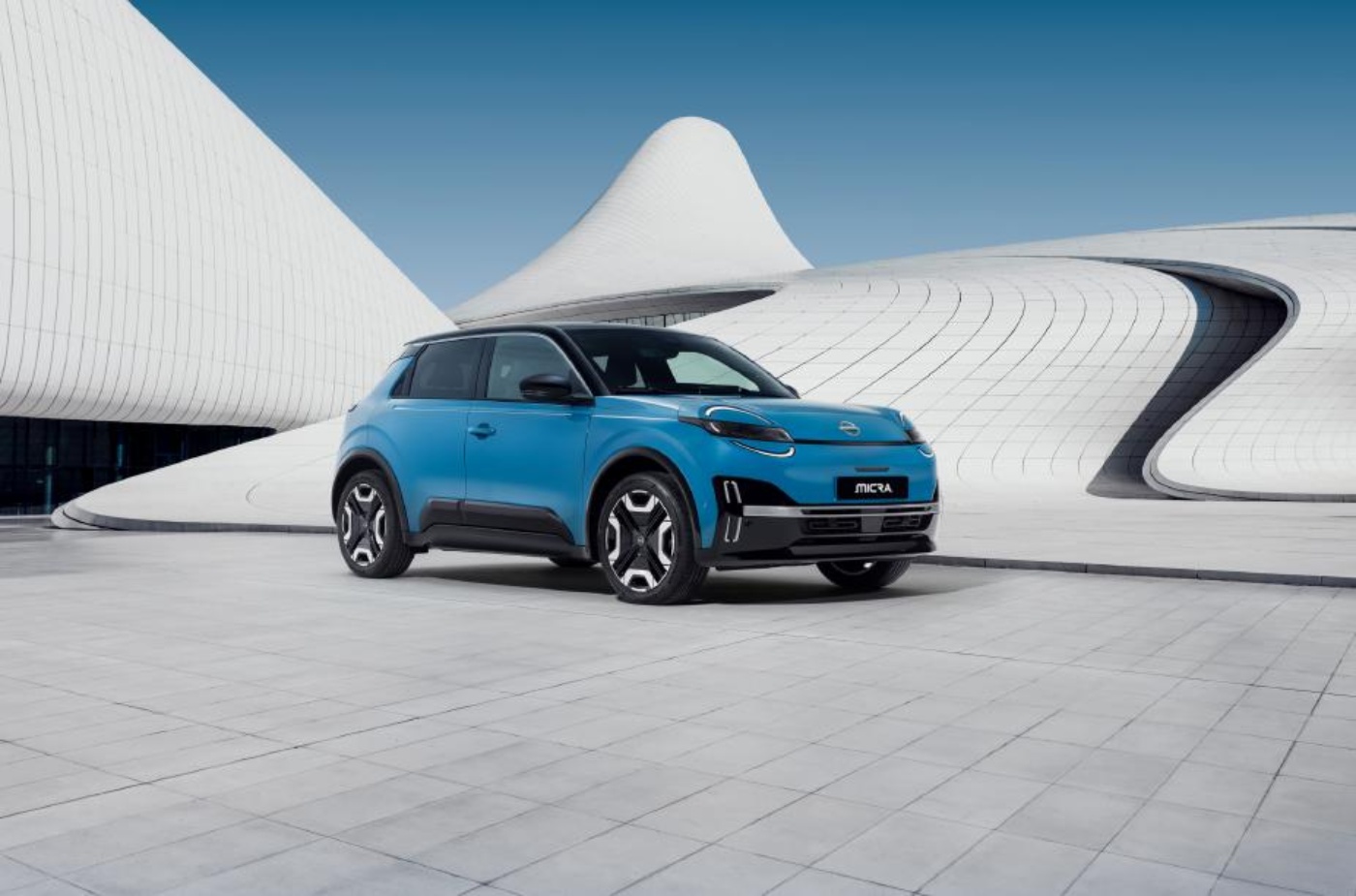 Ein blauer elektrischer Nissan steht vor einem modernen, geschwungenen weißen Gebäude mit futuristischer Architektur.