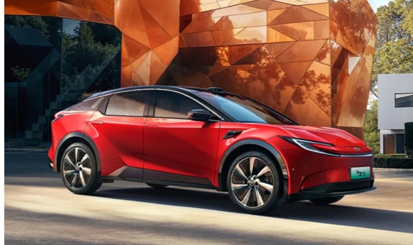 A red electric SUV is parked in front of a modern copper-colored building.