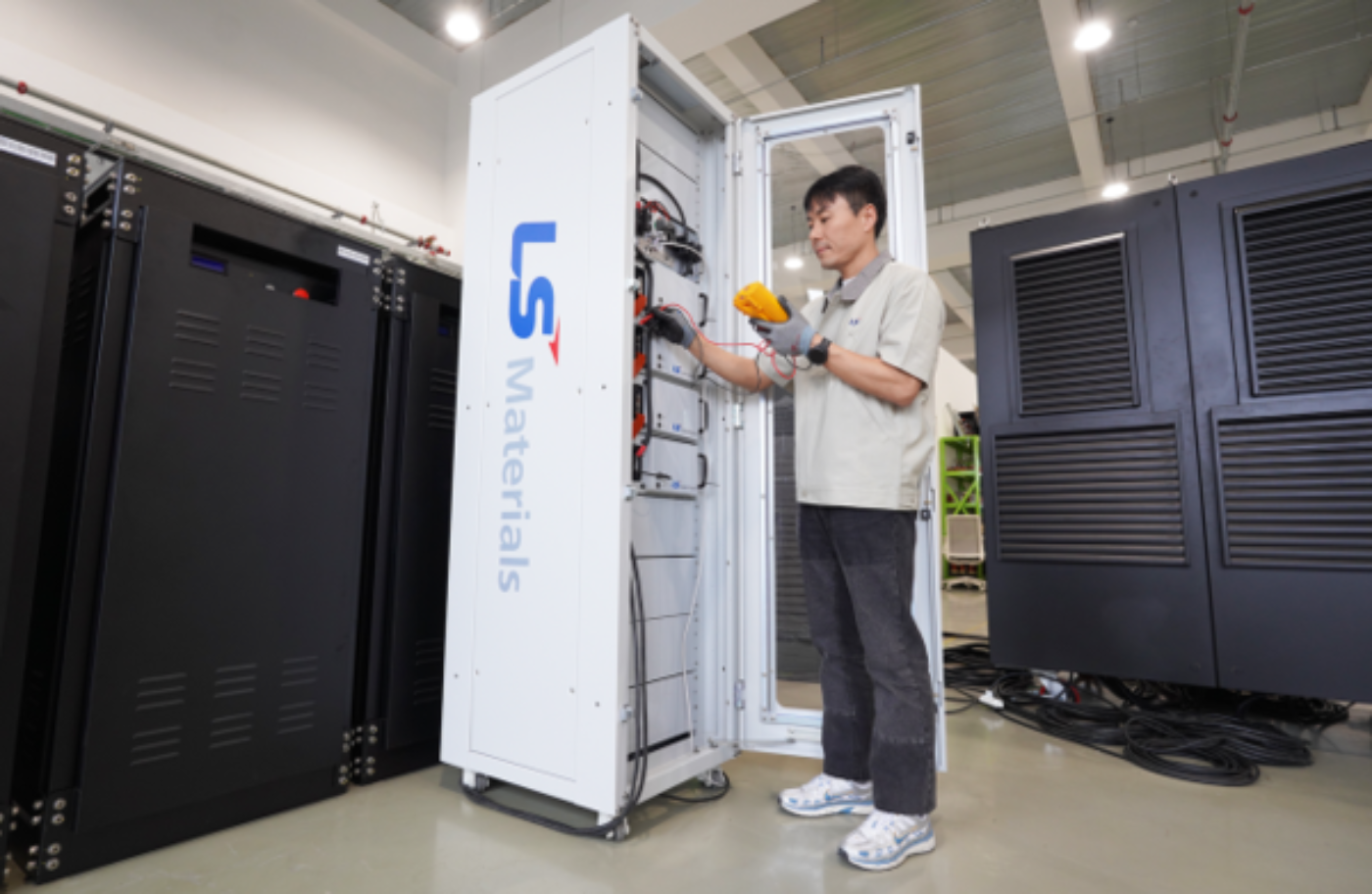 A technician checks electrical components inside an LS Materials cabinet in a server room.