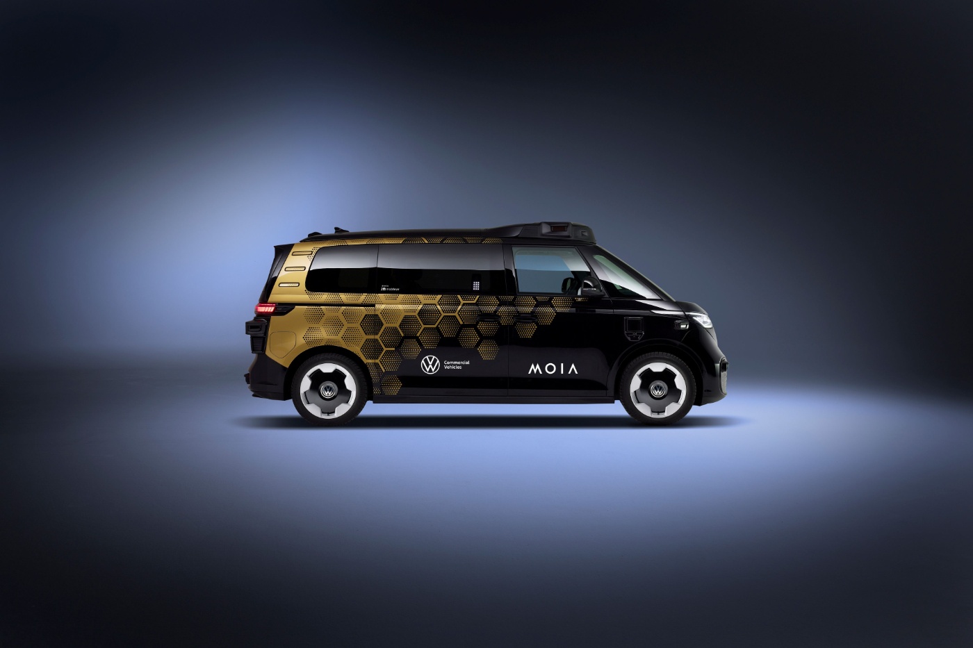 Seitenansicht eines schwarz-goldenen autonomen VW-Vans mit MOIA- und VW-Logos vor dunklem Hintergrund.