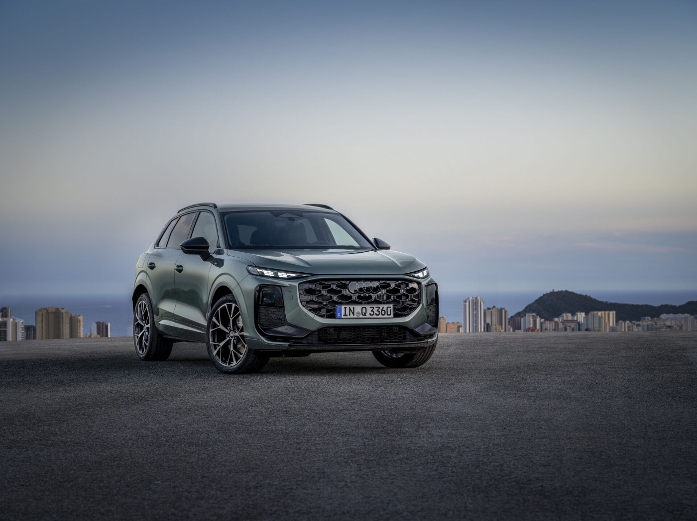 Frontale Seitenansicht eines Audi-SUVs auf freier Fläche mit Skyline und Hügeln im Hintergrund.