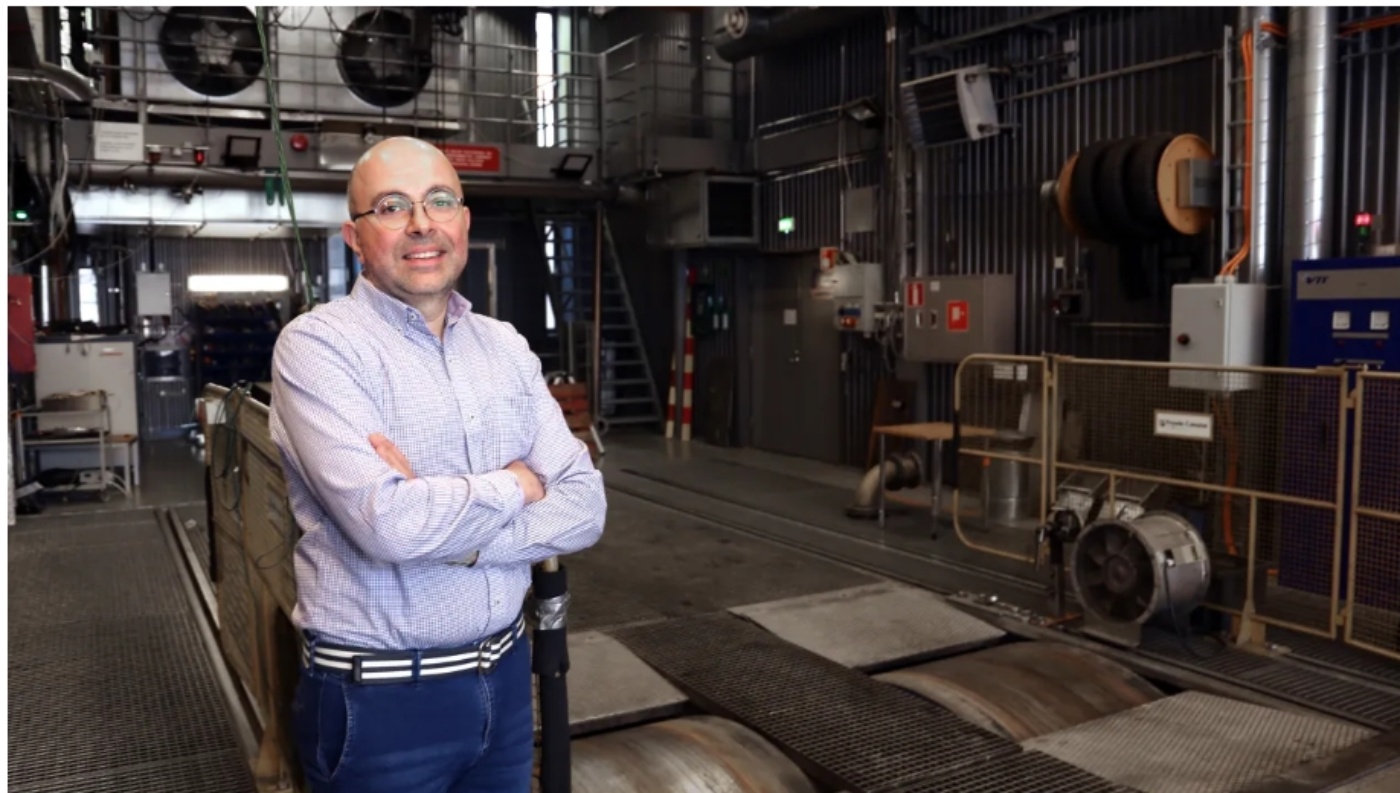 Man standing in an industrial testing facility with large fans and technical equipment in background.