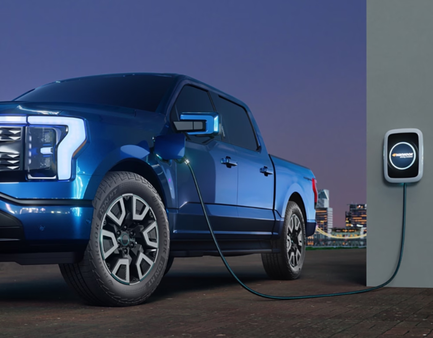 Ein elektrischer Pickup lädt an einer Wandladestation, im Hintergrund ist eine Skyline sichtbar.