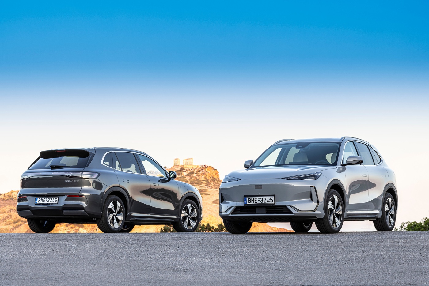 Zwei Elektro-SUVs stehen auf offener Straße, im Hintergrund Hügel und antike Ruinen.