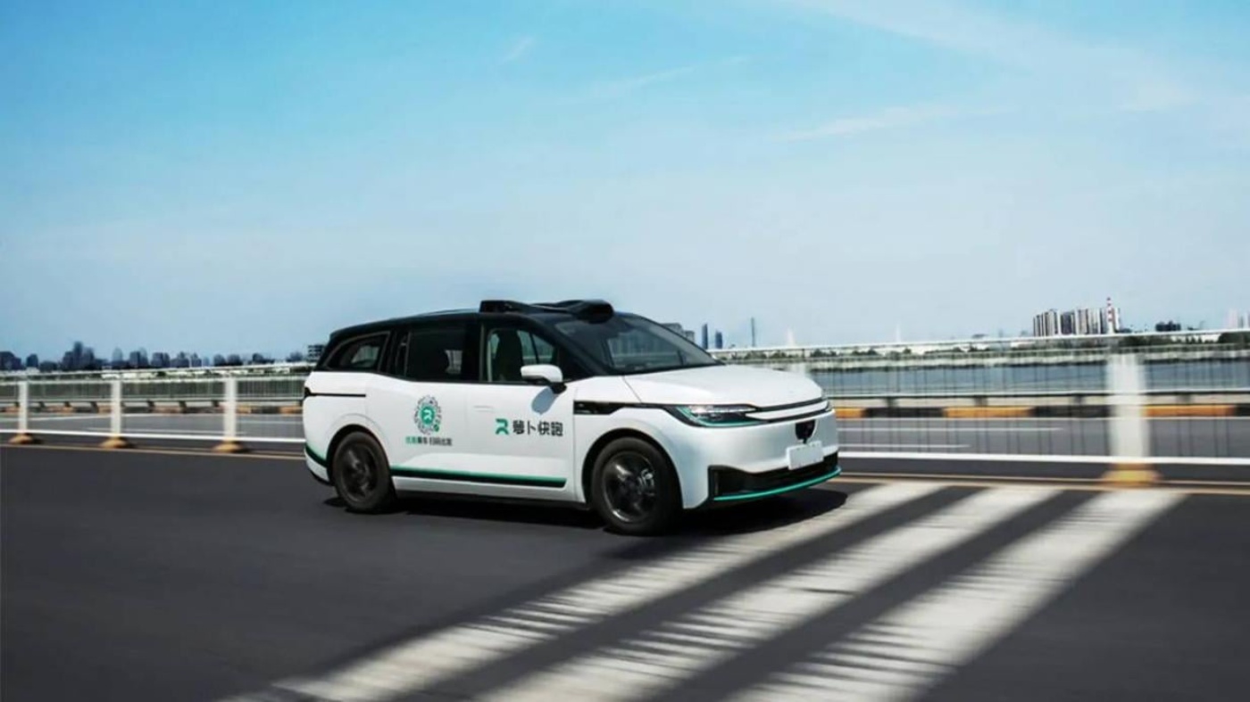 Autonomes Taxi mit chinesischer Beschriftung fährt bei Tageslicht über eine Brücke mit Skyline im Hintergrund.