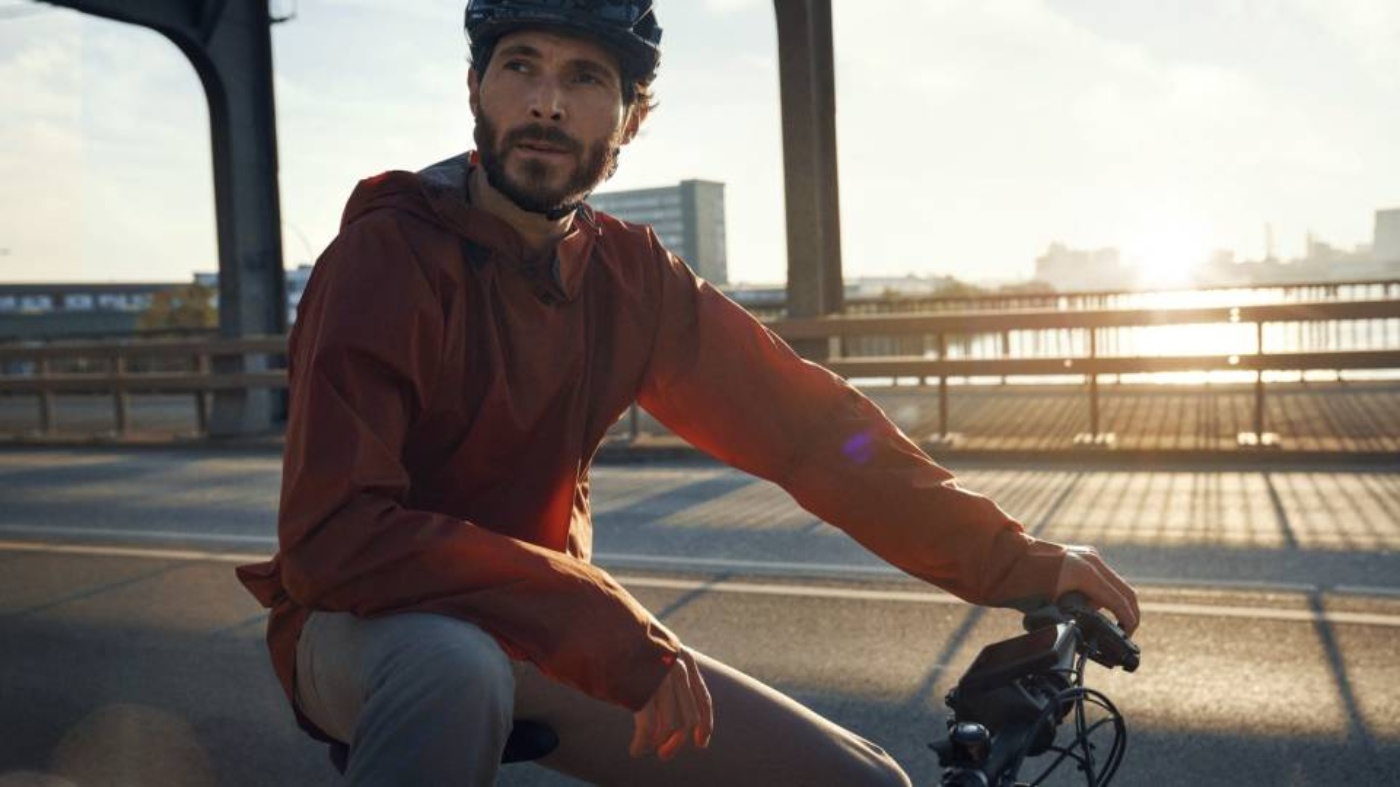 Mann mit Helm fährt bei Sonnenaufgang auf einer Brücke Fahrrad und blickt zur Seite.