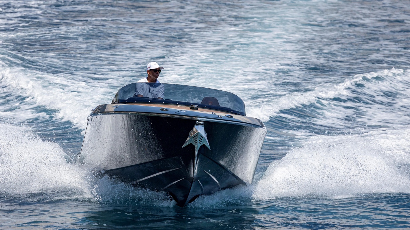 Person fährt ein schwarzes Porsche-Sportboot über das Wasser und erzeugt Wellen.