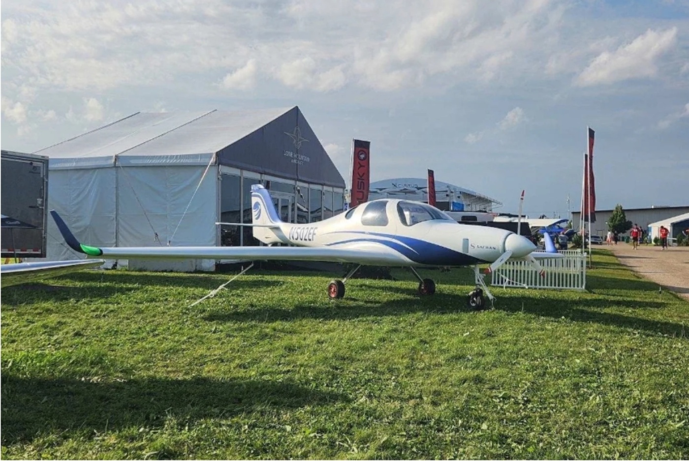 Small white and blue electric airplane on display at an outdoor event.
