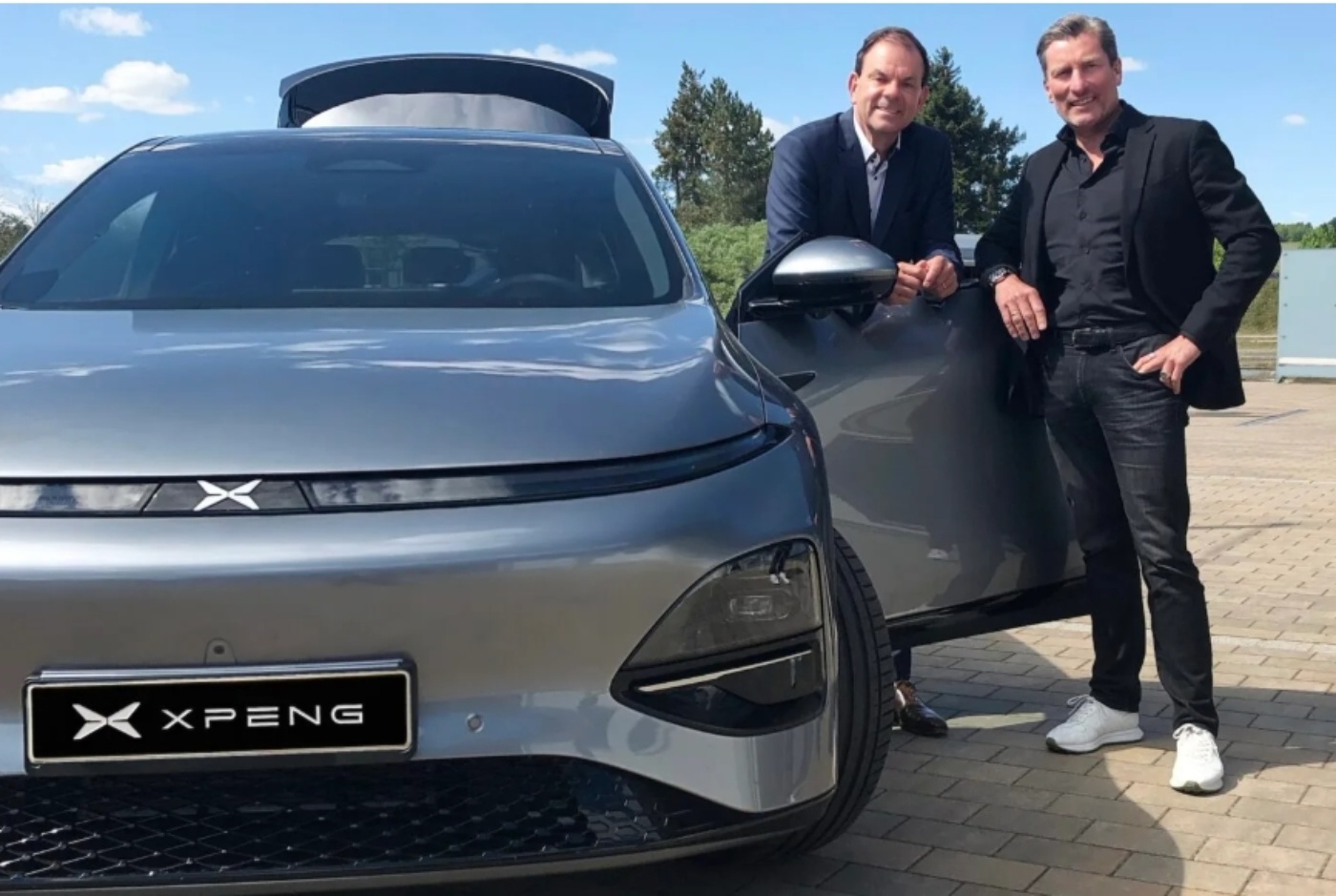 Two men standing beside a silver XPeng electric car with the driver’s door open.