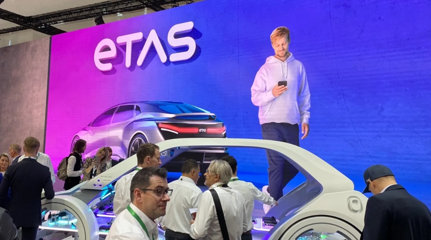 ETAS trade show booth with digital car model and large screen showing a man using a smartphone.